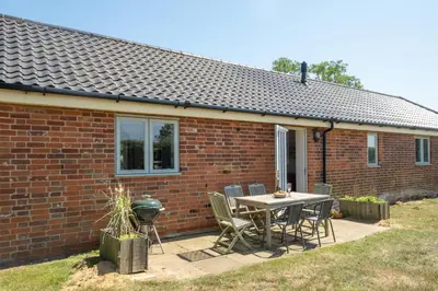 a patio with a table and chairs in front of a brick house at 2 Hazelwood - 2 bedroom house near Aldeburgh & Snape Maltings - Aldeburgh Coastal Cottages in Aldringham
