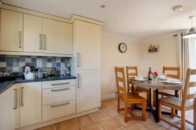 a kitchen with white cabinets and a table and chairs at 2 Hazelwood - 2 bedroom house near Aldeburgh & Snape Maltings - Aldeburgh Coastal Cottages in Aldringham