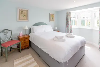 a bedroom with a large white bed and a chair at The Pink House, Thorpeness in Thorpeness