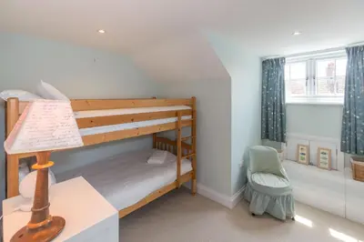 a bunk bed in a room with a lamp and a chair at The Pink House, Thorpeness in Thorpeness
