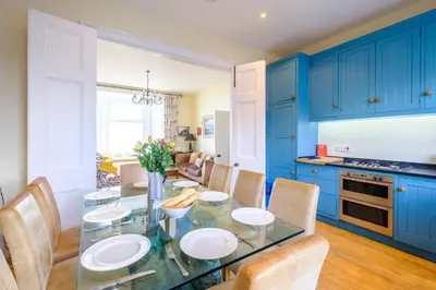 a kitchen with blue cabinets and a glass table and chairs at Gunfleet, Aldeburgh - A Large Seafront House with Stunning Sea Views from all the floors, Sleeps 14 - Aldeburgh Coastal Cottages in Aldeburgh