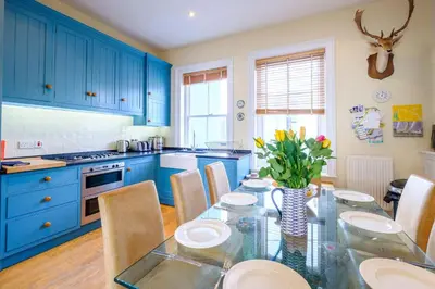 a kitchen with blue cabinets and a table with chairs at Gunfleet, Aldeburgh - A Large Seafront House with Stunning Sea Views from all the floors, Sleeps 14 - Aldeburgh Coastal Cottages in Aldeburgh