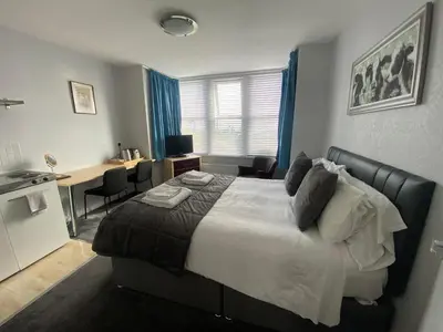 a bedroom with a large bed with a desk and a kitchen at WynnStay Studio Apartments in Southend-on-Sea