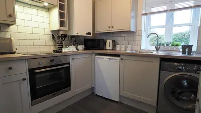 a kitchen with white cabinets and a washer and dryer at Woodlands View in Halesworth