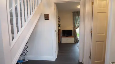 a hallway with a white staircase and a television at Hideaway Cottage in Halesworth