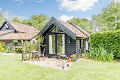 a small black cottage with a grill in the yard at Garden Cottage in Diss