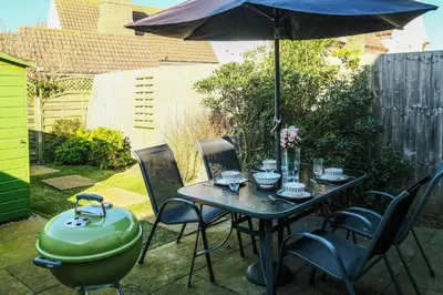 a table and chairs with an umbrella and a grill at Pinky Cottage in Aldeburgh