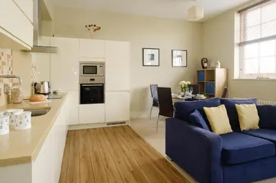 a living room with a blue couch and a kitchen at Beachcomber - Aldeburgh Coastal Cottages in Aldeburgh