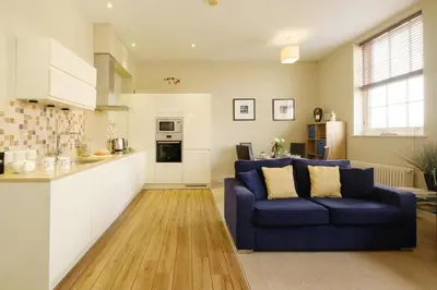 a living room with a blue couch and a kitchen at Beachcomber - Aldeburgh Coastal Cottages in Aldeburgh
