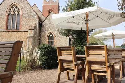 a table and chairs with an umbrella and a church at The Bell Inn in Thorpe le Soken