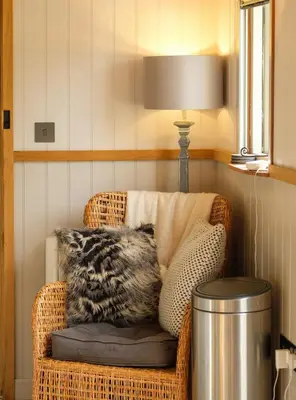 a wicker chair with a pillow and a lamp at Piano Forte - a delightful rural shepherd hut & hot tub available ! in Rushford