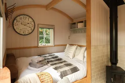 a bedroom with a bed with a clock on the wall at Piano Forte - a delightful rural shepherd hut & hot tub available ! in Rushford