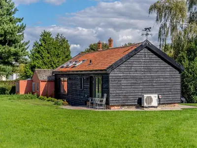 a small black house in a field of grass at Blackwell Barn in Raydon