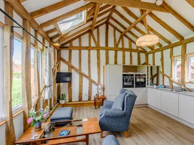 a large living room with wooden ceilings and windows at Blackwell Barn in Raydon