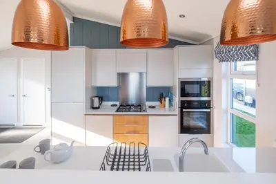 a kitchen with white cabinets and orange pendant lights at Sea Breeze - Aldeburgh Coastal Cottages in Sizewell