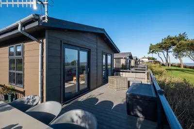 a black tiny house with a deck with chairs at Sea Breeze - Aldeburgh Coastal Cottages in Sizewell