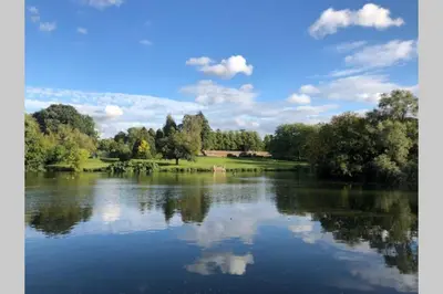 a view of a lake with trees and clouds at Little Easton Manor in Great Easton