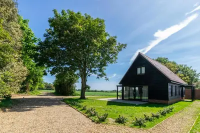 a small black house in a field with a tree at 1 Bed in Sudbourne oc-tgs in Sudbourne