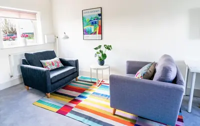 a living room with two chairs and a colorful rug at Elm Cottage at Gravel Farm in Stretham