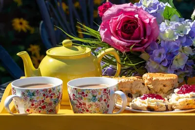 two cups of tea and some cakes and flowers at Stylish Town Centre House with Garden and Parking Opposite in Bury Saint Edmunds