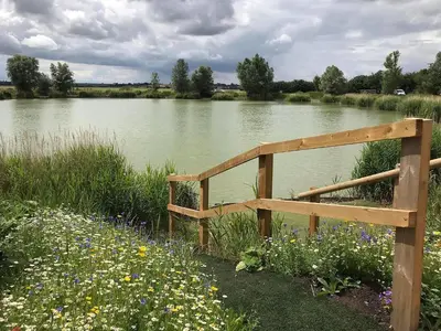 a wooden fence in front of a river with flowers at Hare Lodge - Uk30604 in Pidley
