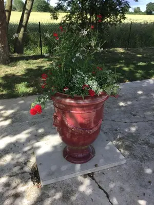 a large red pot with flowers in it on a stand at wingate cottage in Southburgh
