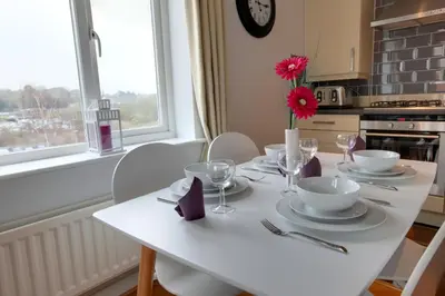 a white table with plates and bowls and a vase with a flower at Modern Spacious Apartments in Bishops Stortford