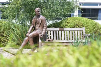 a statue of a man sitting on a bench at Christ's College Cambridge in Cambridge