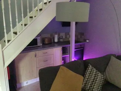 a living room with a couch and a kitchen under a staircase at The Bakehouse in Harwich