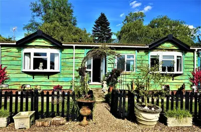 a green house with a fence in front of it at Lakeland Lodge with private Hot Tub and fishing in Hatfield Peverel