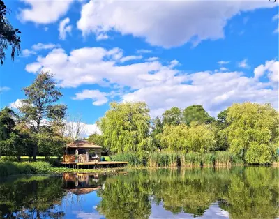 a boat on a lake with a blue sky and clouds at Lakeland Lodge with private Hot Tub and fishing in Hatfield Peverel