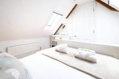 a white bedroom with two white slippers on a bed at Mansard House in Aldeburgh