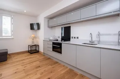 a kitchen with white cabinets and a wooden floor at Three Tuns Apartments - Hazel - Aldeburgh Coastal Cottages in Pettistree