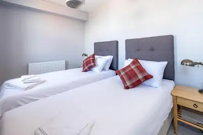 two beds in a bedroom with white sheets and red pillows at Crags Nest in Aldeburgh