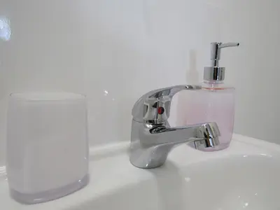 a bathroom sink with a soap dispenser and a glass at The Cambridge Suites - Tas Accommodations in Cambridge