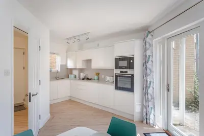 a white kitchen with white cabinets and blue chairs at 2 Bedroom City Centre Townhouse - with Parking in Cambridge