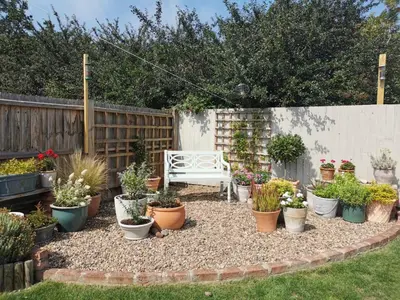 a garden with potted plants and a white bench at The Garden Room in Leiston