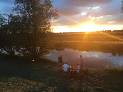 a group of people sitting around a table by a lake at Chestnut Cottage at Gravel Farm in Stretham