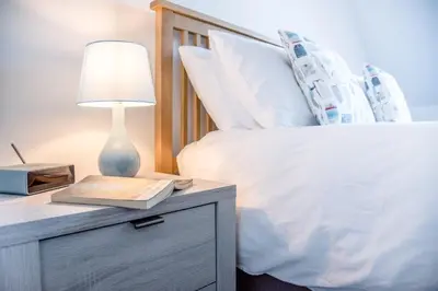 a bed with a nightstand with a lamp and a book at 3 Oaks Court, Thorpeness in Thorpeness