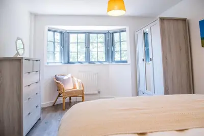 a bedroom with a bed and a chair and windows at 3 Oaks Court, Thorpeness in Thorpeness