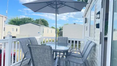 a table and chairs on a porch with an umbrella at Excellent caravan 2 bedrooms sleeps 6 in East Mersea