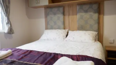 a bed with white sheets and pillows in a room at Excellent caravan 2 bedrooms sleeps 6 in East Mersea
