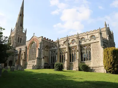 an old church with a tower on a grass field at Flink's Barn in Great Dunmow