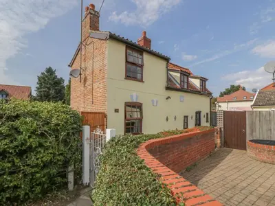 a white house with a brick wall and a fence at Rose Cottage in Ipswich