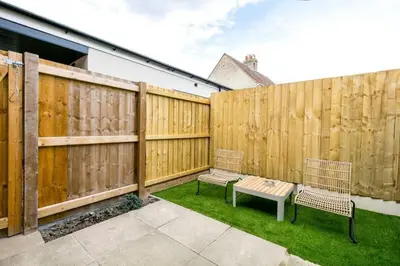 a patio with two chairs and a bench in front of a fence at Spacious Modern Garden Family Home in Cambridge