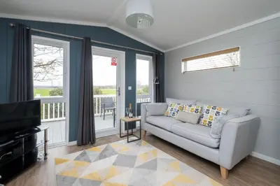 a living room with a couch and a television at Savannah Lodge - Aldeburgh Coastal Cottages in Sizewell