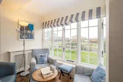 a living room with two chairs and a table and windows at Sanctuary House in Thorpeness