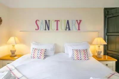 a bedroom with a white bed with a saturday sign on the wall at Sanctuary House in Thorpeness