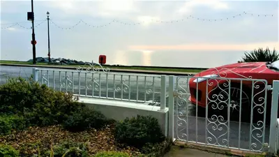a red car is parked next to a fence at Beachfront Studio Apartment in Felixstowe