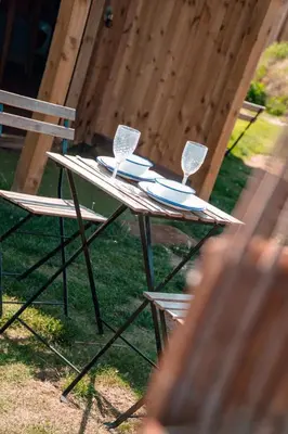 a picnic table with two wine glasses and a chair at Hatters Meadows Glamping in Ely